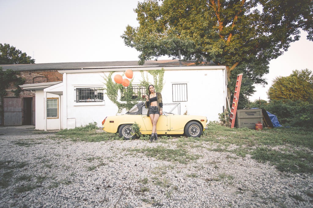 Figure with orange balloons leaning on a yellow convertible