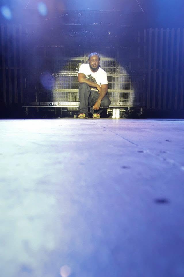 T-Pain crouched at the back of the stage in a spotlight