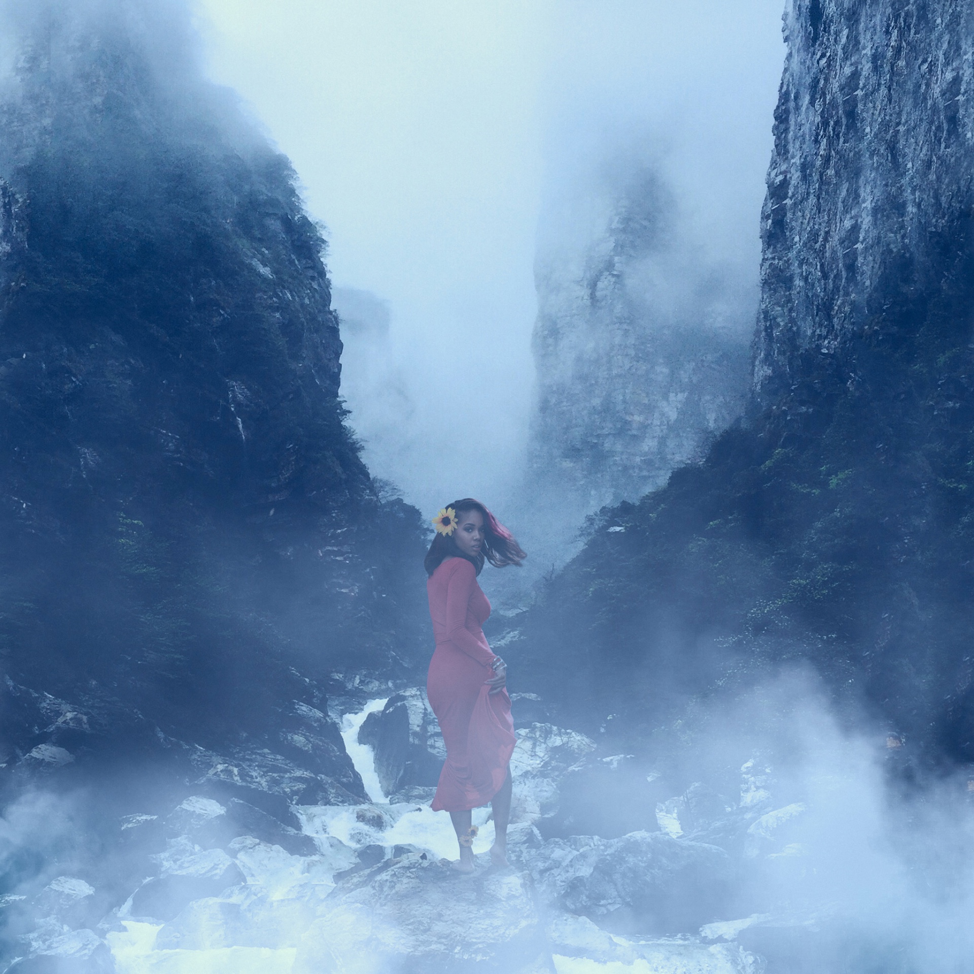 Figure in a red dress standing among misty canyon cliffs