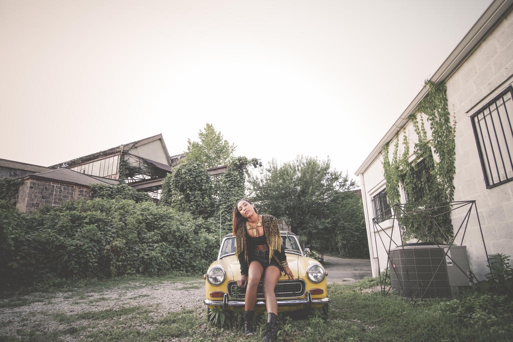 Figure resting on a vintage yellow car amid overgrown ruins