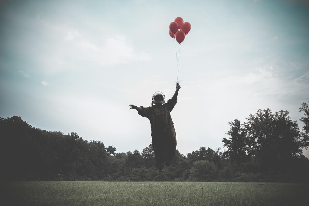 Helmeted figure lifted skyward by red balloons in a field